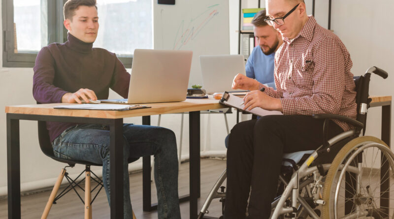 grupa mężczyzn pracujących razem w biurze z osobą na wózku inwalidzkim