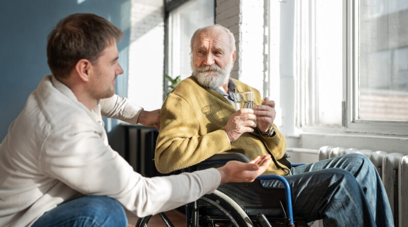 młody mężczyzna pochyla się nad starszym panem na wózku inwalidzkim