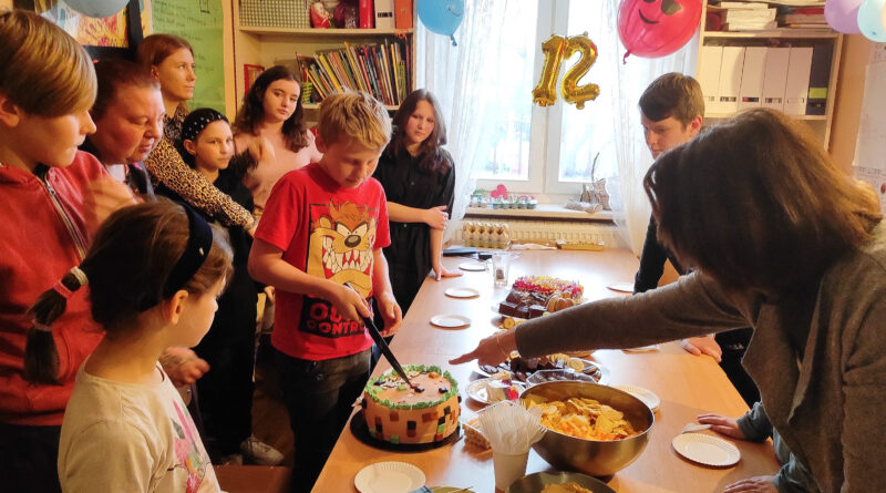 grupa osób dzieci i dorosłych stoi przy stole z tortem